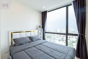 A modern hotel room with a large bed, a headboard with gold trim, a nightstand, and a view of the city through large windows. - Bilik Selesa Tingkat Tinggi dengan Pemandangan Sungai Chao Phraya Mempesonakan (Chang Wat Nonthaburi)