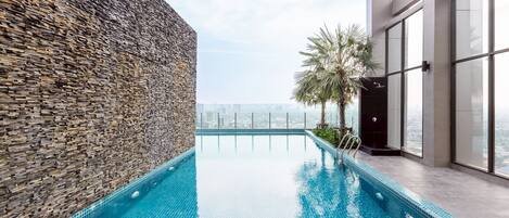 Una piscina infinita en la azotea, con una pared de piedra y un edificio moderno de vidrio.