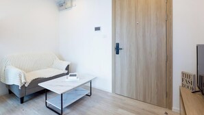 A room with a grey sofa, a white coffee table, a wooden wardrobe, and a television on a wooden stand.