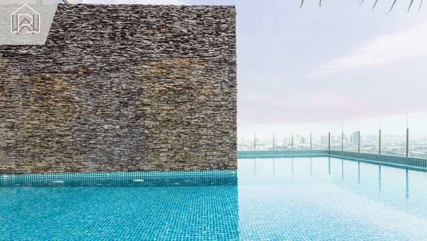 A swimming pool with a stone wall and a city skyline view.
