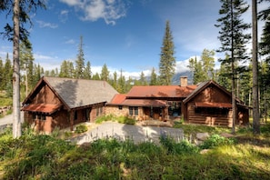 Une cabane rustique, dotée de fondations en pierre, d’un revêtement extérieur en bois et d’un toit en métal, et entourée d’un paysage boisé.