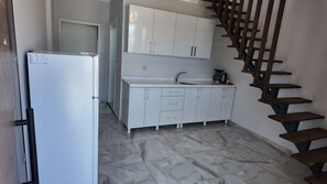 Une cuisine avec des meubles blancs, un réfrigérateur, un évier et un sol carrelé en marbre.