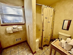Un baño con cortina de ducha, inodoro, ventana con persianas y un perchero para toallas.