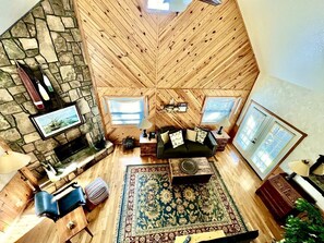 A loft-style living room with a stone fireplace, wooden ceiling, and large windows.