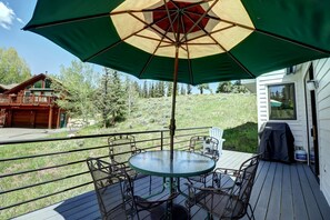 A deck with a round glass table and chairs, an umbrella, and a grill.