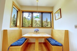 A room with a wooden table and bench seating, a window with a view of trees, and a hanging light fixture.