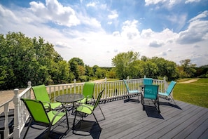Una terraza con mobiliario exterior, baranda blanca y vista a un área verde con árboles.