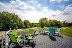 Een terras met buitenmeubilair, een witte balustrade en uitzicht op een gazon met bomen.