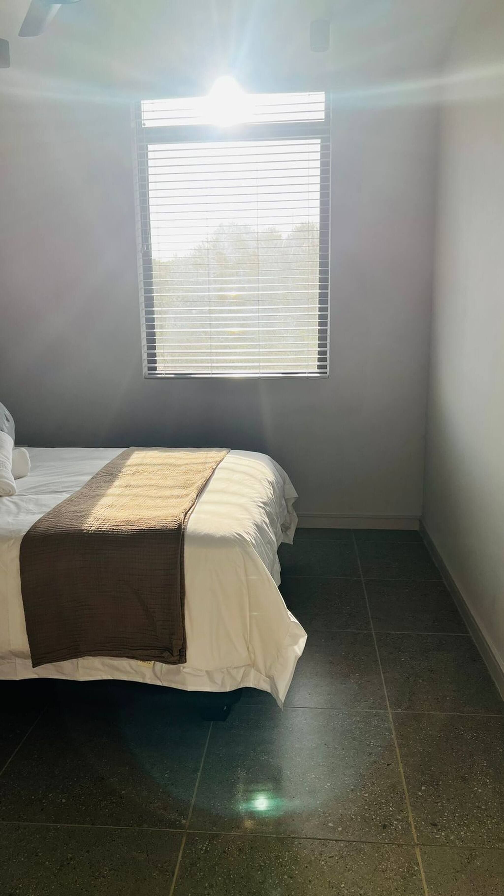 Ein Schlafzimmer mit Bett, Fenster mit Jalousien und Fliesenboden.