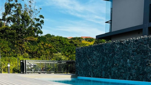 A wooden deck leading to a swimming pool with a stone wall and a modern building in the background. - Zimbali Lakes Boulevard Edge 214 (Ballito)