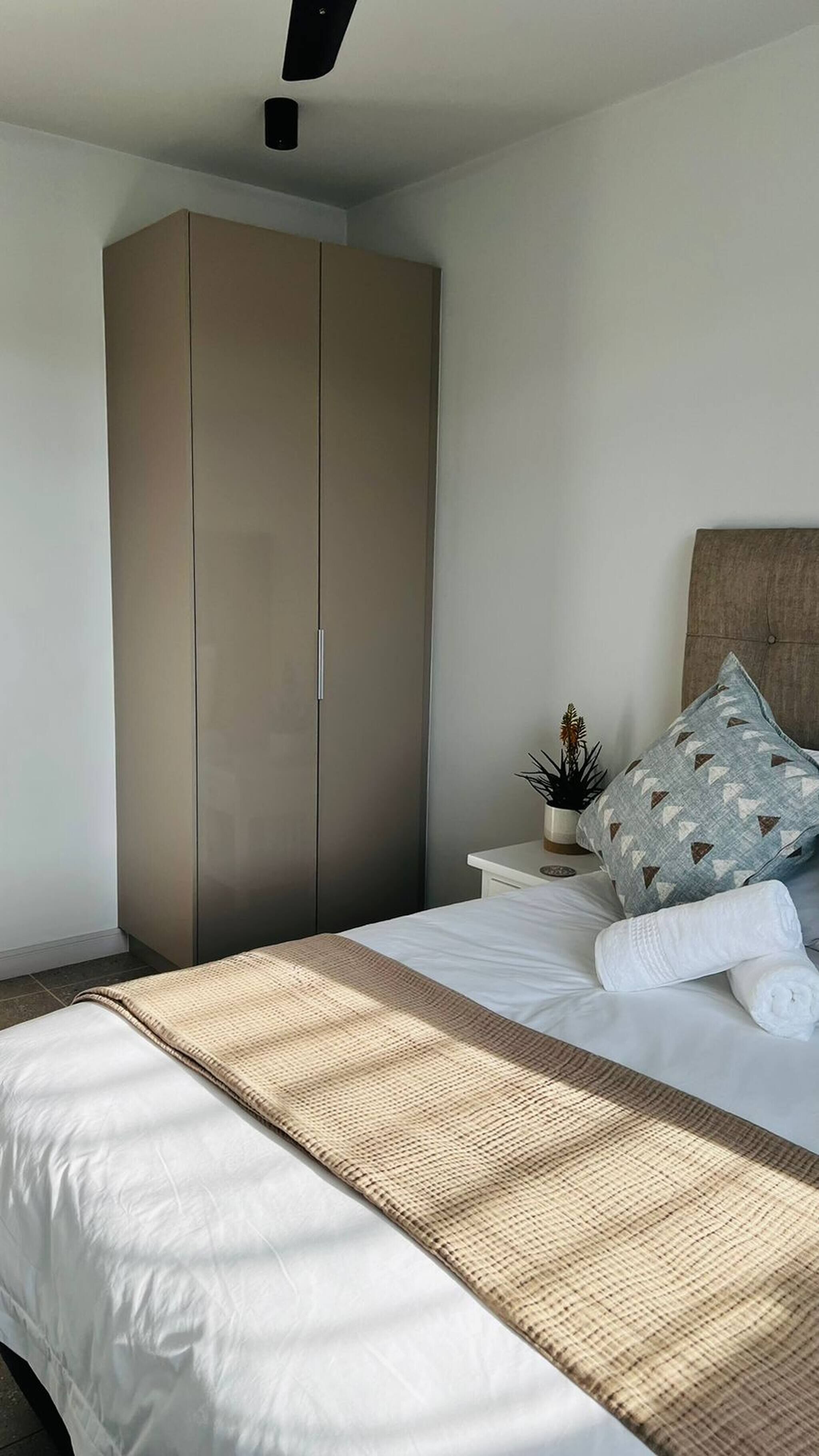 A bedroom with a bed, a wardrobe, a nightstand, and a ceiling fan.