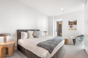 Ein modernes Schlafzimmer mit einem großen Bett, Nachttischlampen, einem kleinen runden Tisch und einem Stuhl.