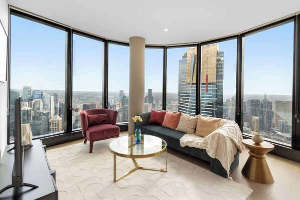 Ein modernes Wohnzimmer mit Sofa, Sessel und Couchtisch, mit Blick auf die Stadt durch große Fenster.