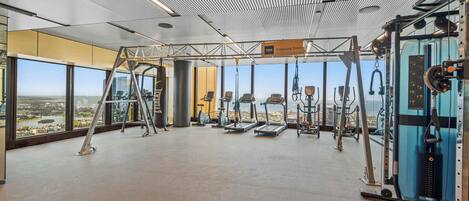 A spacious gym with various exercise equipment, large windows offering a view of the city, and a 'Training Zone' sign.