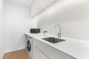 Ett modernt kök med inbyggd tvättmaskin, mikrovågsugn och en diskho i rostfritt stål.