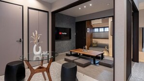 Een moderne woonkamer met een eettafel met glazen blad, een bank en een aan de muur bevestigde televisie.