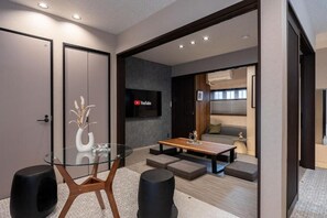 A modern living room with a glass-top dining table, a sofa, and a TV mounted on the wall. - JAPAVISTA Zen (YOSHINO, FUKUSHIMA WARD)