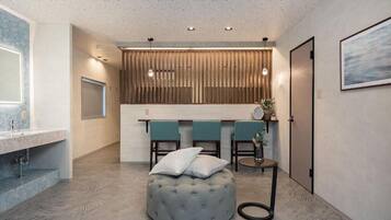 A modern bathroom with a marble countertop, a round ottoman, and a wooden panel wall.