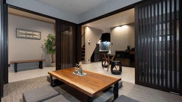 Een modern interieur met een houten eettafel, een bankje en een trap naar een keukenhoek.