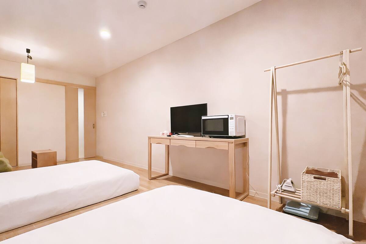 A hotel room with two beds, a desk with a TV and microwave, a chair, and a wardrobe.