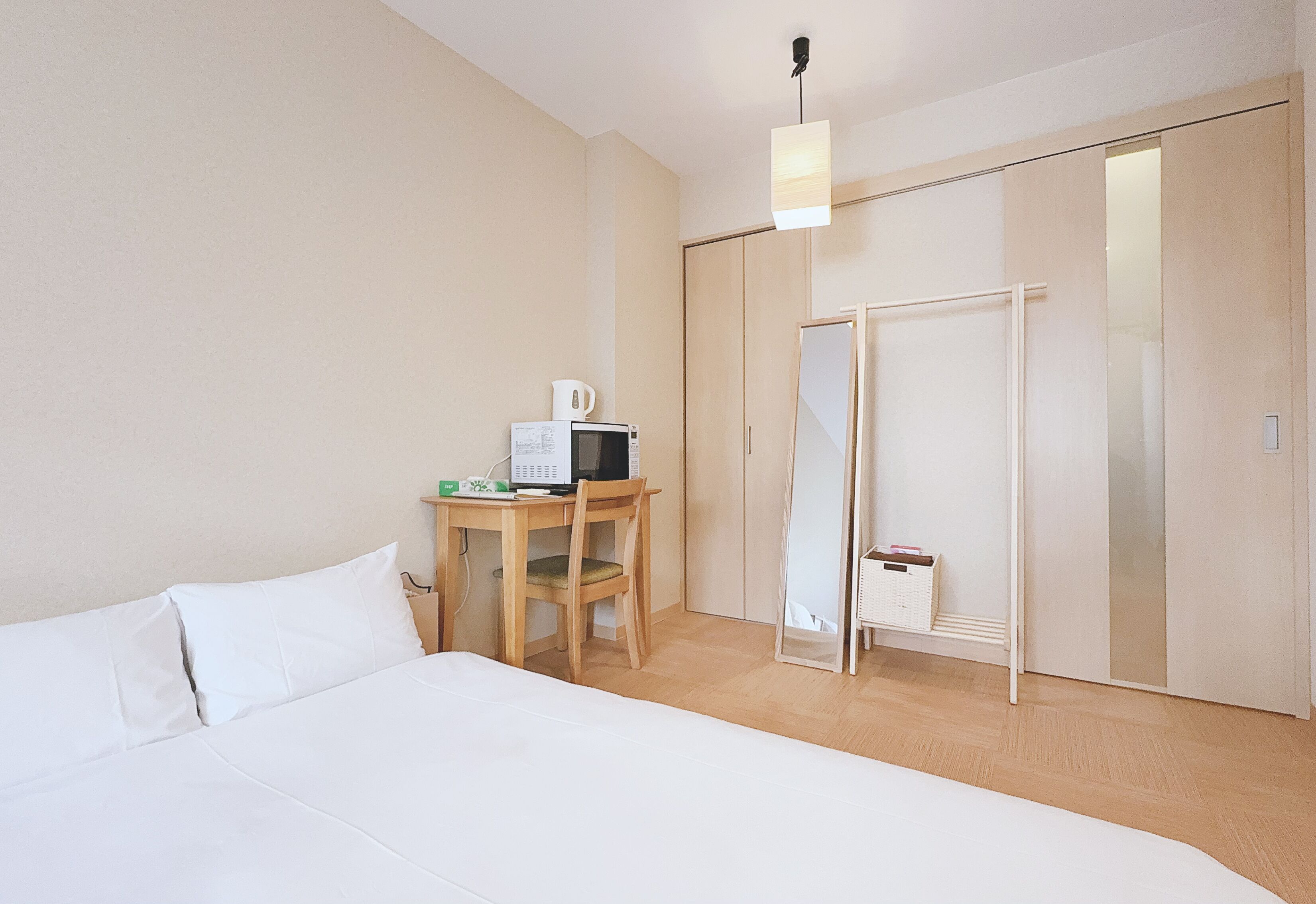 A bedroom with a bed, a desk with a computer, a microwave, and a closet.