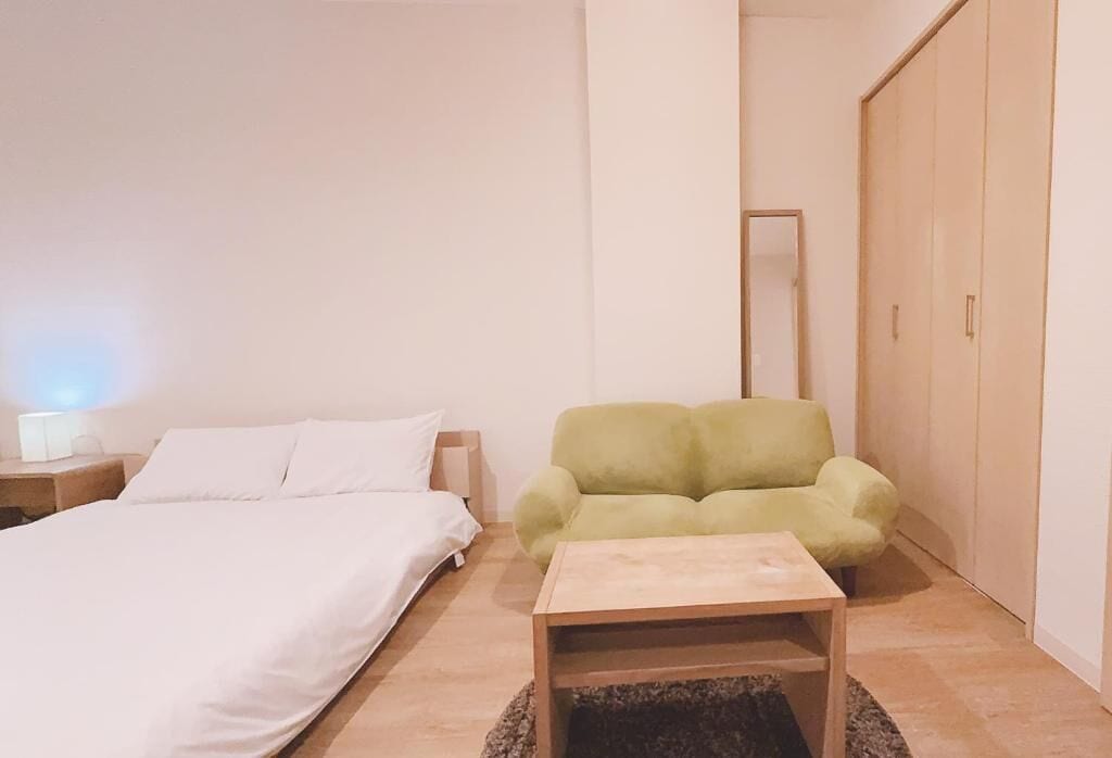 Una camera da letto con un letto, una poltrona verde, un comodino in legno e uno specchio a parete.