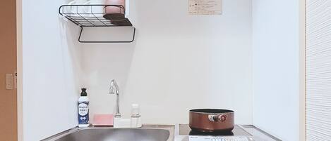 A compact kitchenette with a sink, a small stove, a microwave, and a storage shelf.