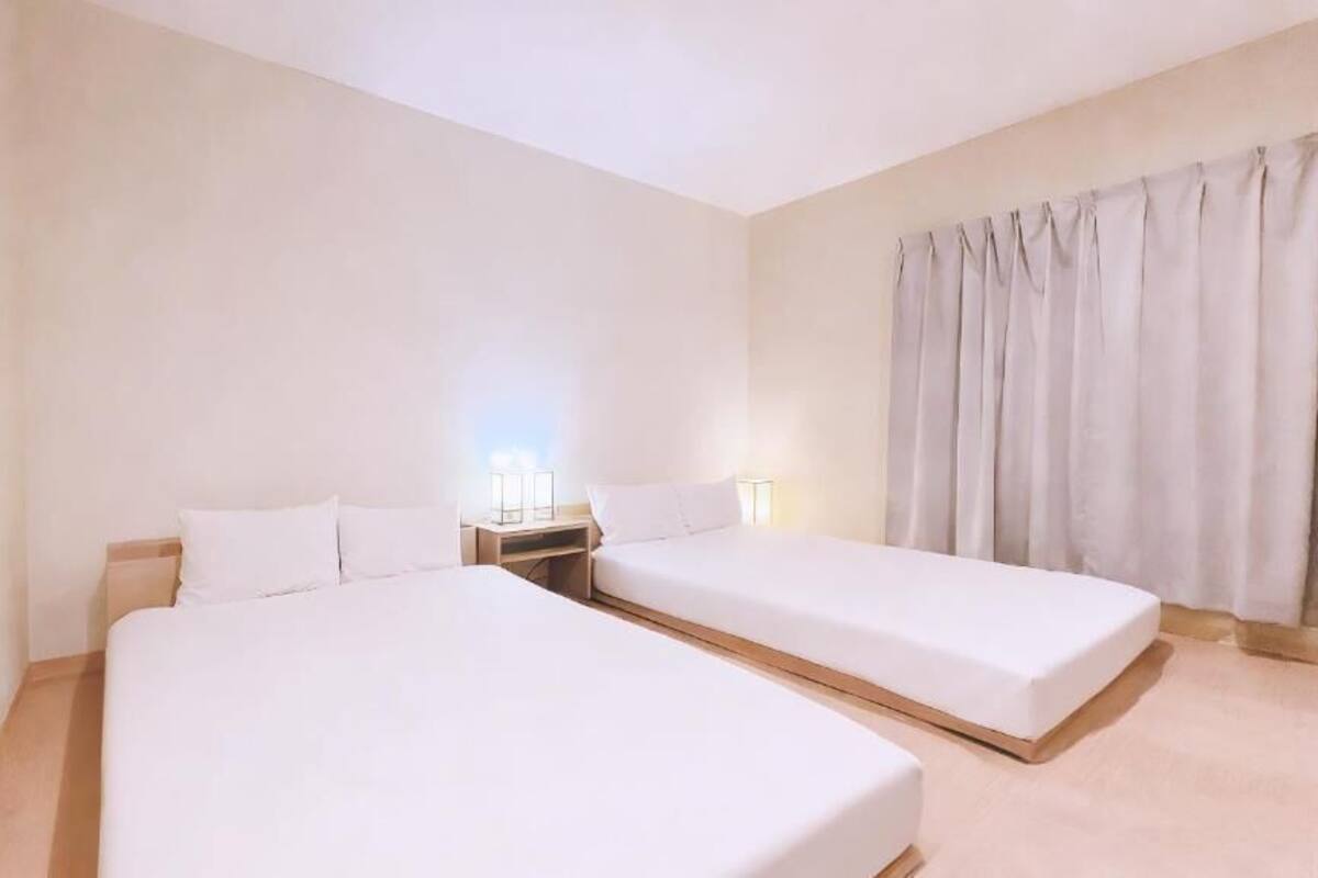 A hotel room with two beds, a nightstand, and a window with curtains.