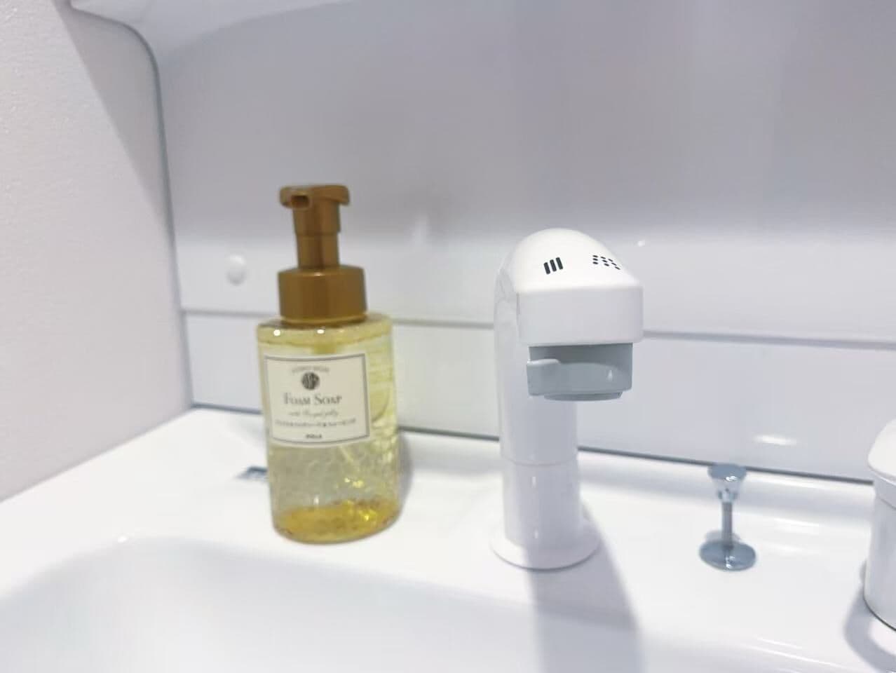 A bathroom sink with a bottle of foam soap and a soap dispenser.