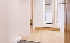 Un pasillo con piso de madera, una puerta blanca y vista a una habitación con refrigerador blanco.