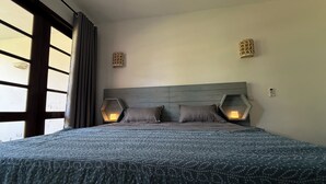 Ein Schlafzimmer mit einem großen Bett, zwei Wandlampen und einem mit Vorhängen versehenen Fenster.