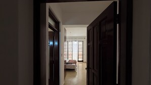 Ein Flur, der zu einem Schlafzimmer mit Bett, Fenster mit Vorhängen und einer Tür führt.
