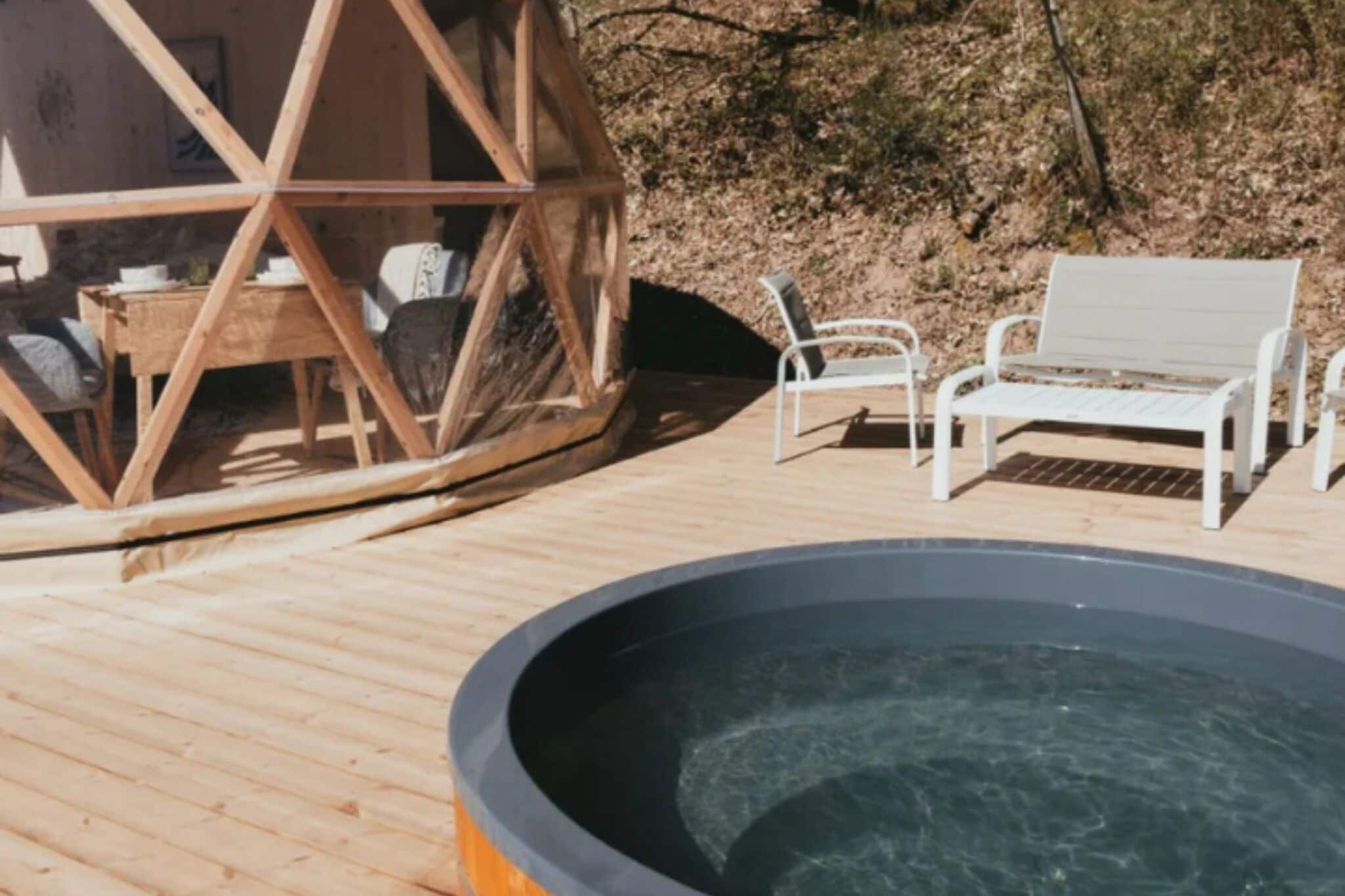 Une terrasse en bois avec un jacuzzi, des chaises en métal blanc et une structure en bois.