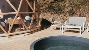 A wooden deck with a hot tub, white metal chairs, and a wooden structure.