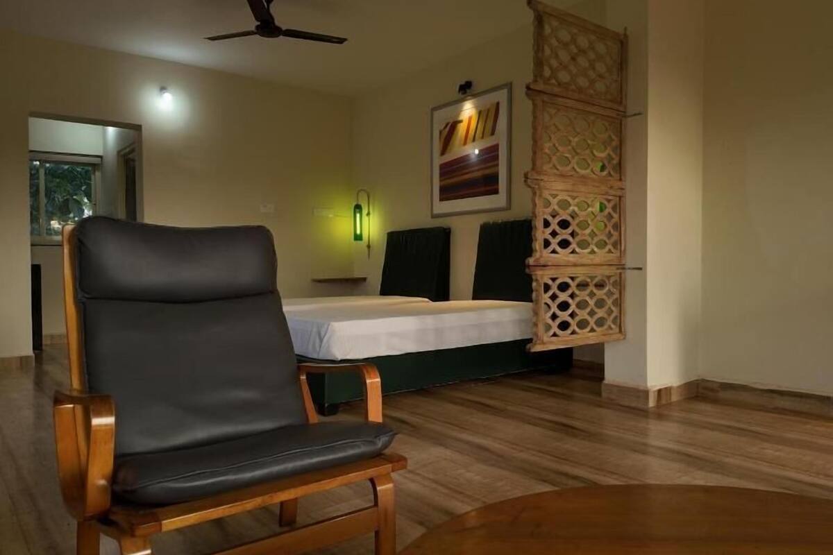 A room with a bed, a chair, a table, a ceiling fan, and a wall-mounted shelf.