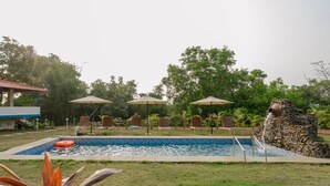 A swimming pool with lounge chairs and umbrellas, surrounded by greenery. - 360 Agonda (Canacona)