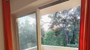 A room with a sliding glass door leading to a balcony with wooden flooring and two yellow chairs. - 360 Agonda (Canacona)