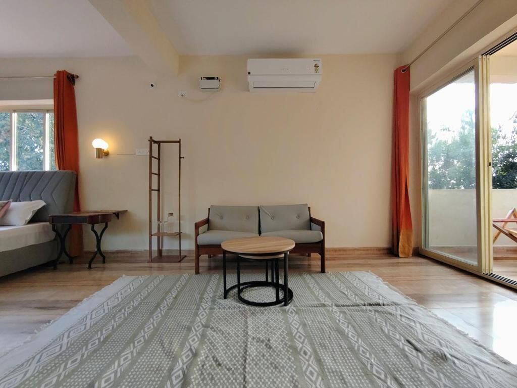 A room with a sofa, a small table, a patterned rug, a ladder, and an air conditioning unit.