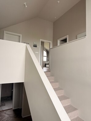A staircase with a white handrail leading to a landing, a door on the left, and a window with curtains in the background. - Charming Holiday House in Álftarnes Iceland with Scenic Views (Álftarnes)