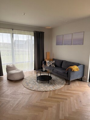 A modern living room with a grey sofa, a round coffee table, a beige bean bag chair, and a patterned rug.