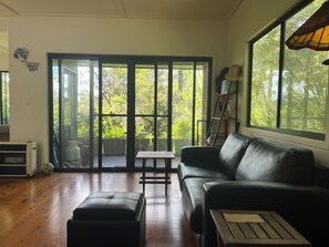 Ein Wohnzimmer mit einer schwarzen Ledersofa, einem Holztisch und einer Glastür, die zu einem Außenbereich mit einer Terrassentisch und Stühlen führt.