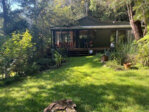 Ein Haus mit Veranda, umgeben von üppiger Vegetation und einem grünen Rasen.