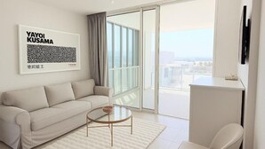 A modern living room with a sofa, a coffee table, a chair, a large window with a view, and a framed artwork on the wall. - Ocean's Edge Suite at 42 Eilat (Eilat)