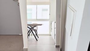 A hallway with a white door, a white wall, and a view into a room with a table and chairs. - Ocean's Edge Suite at 42 Eilat (Eilat)