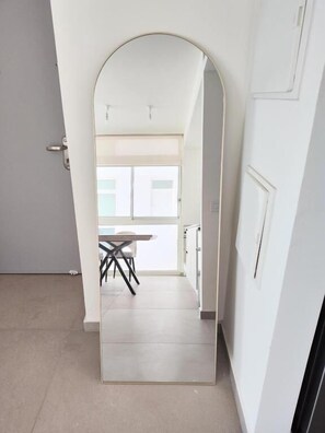 Um corredor com uma porta e uma parede brancas, e vista para um quarto com mesa e cadeiras.