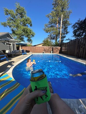 A swimming pool with a person in the water, a can of Twisted Tea, and a blue umbrella.