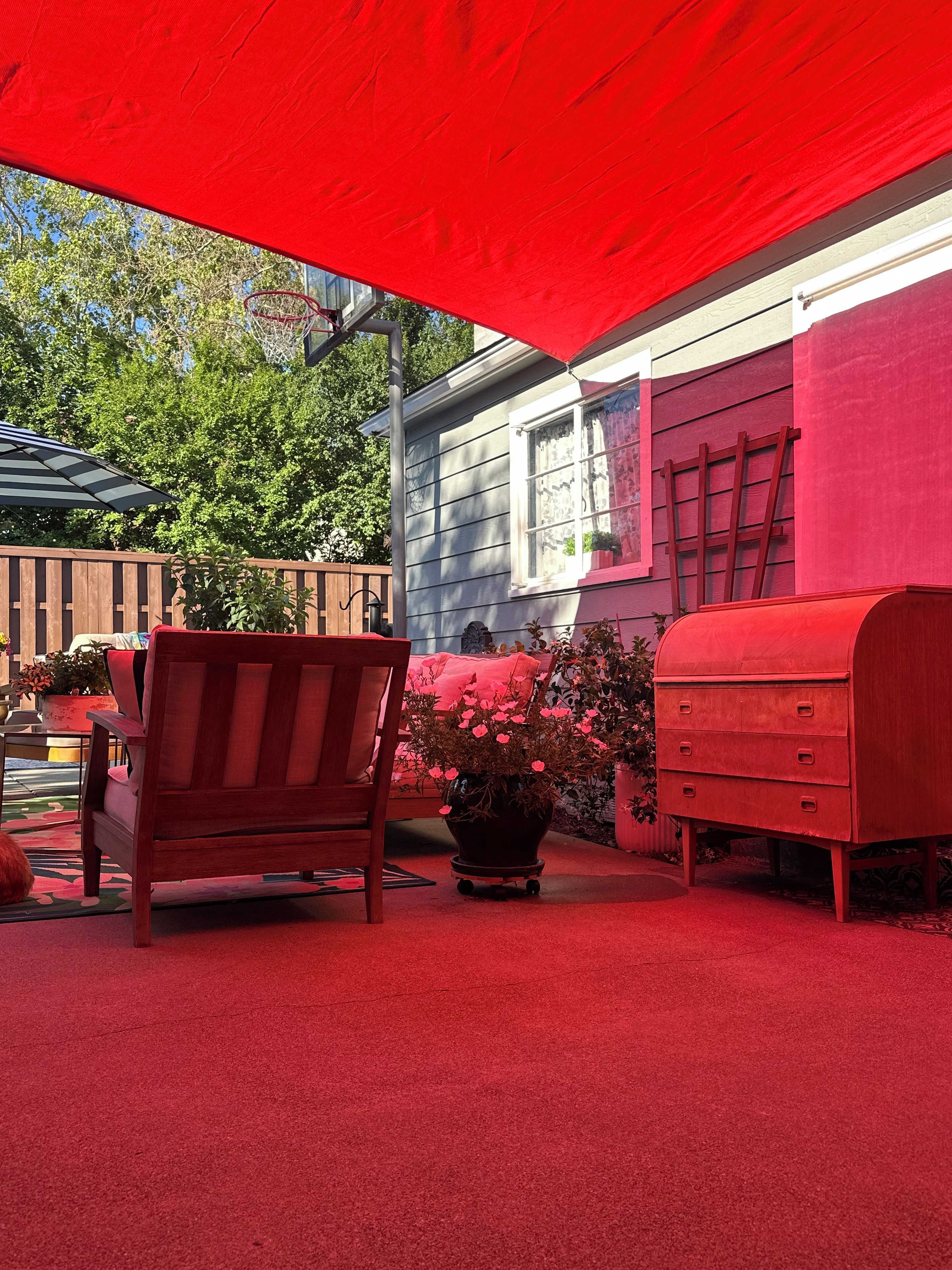 A red outdoor seating area with a wooden chair, a red mailbox, and a potted plant.