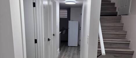 A hallway with a wooden staircase, white walls, and a ceiling light.