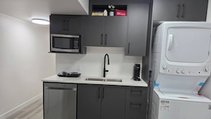 A compact kitchen with a microwave, coffee maker, dishwasher, and a white washing machine. - The Cozy Corner HOme (Winnipeg)