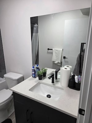 Een moderne badkamer met een wit wastafelmeubel, zwarte kastjes, een toilet en een douchegordijn.